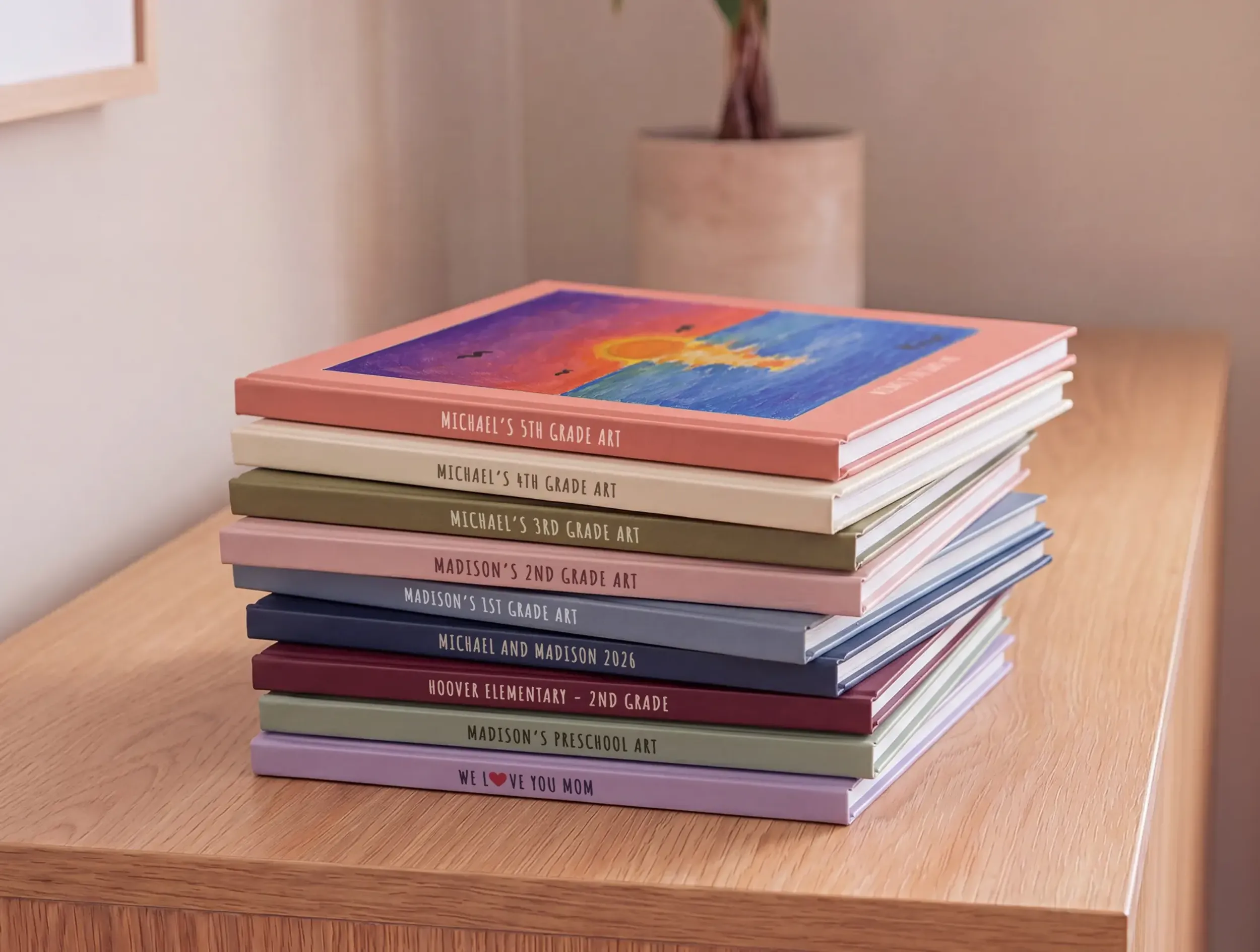 A stack of kids art books on a shelf, one for every grade from preschool through 5th grade, topped with a child's painted sunset artwork