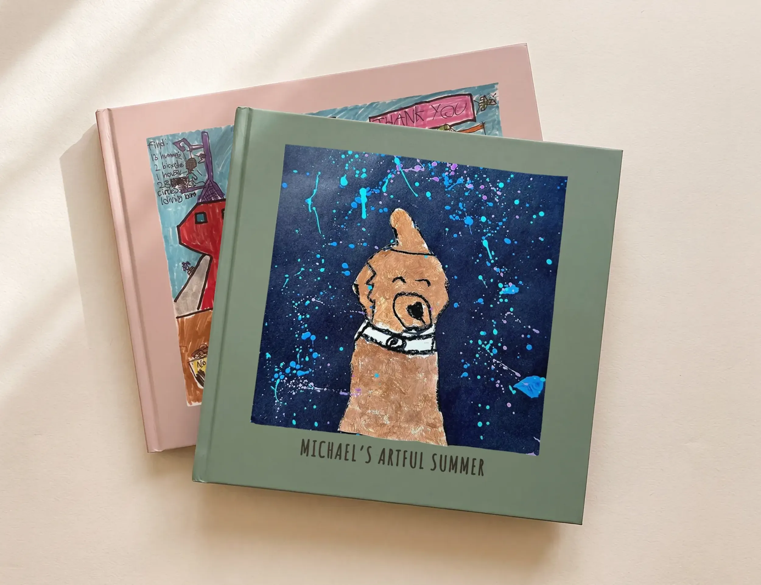 Two kids art books, one with a child's painted dog on a starry night background, another with a crayon house and neighborhood scene