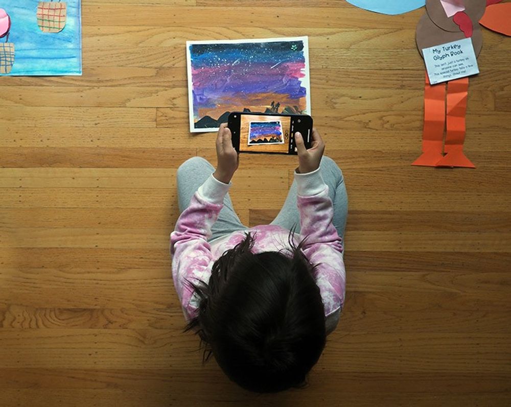 A child taking a photo of her artwork to be uploaded into her art book
